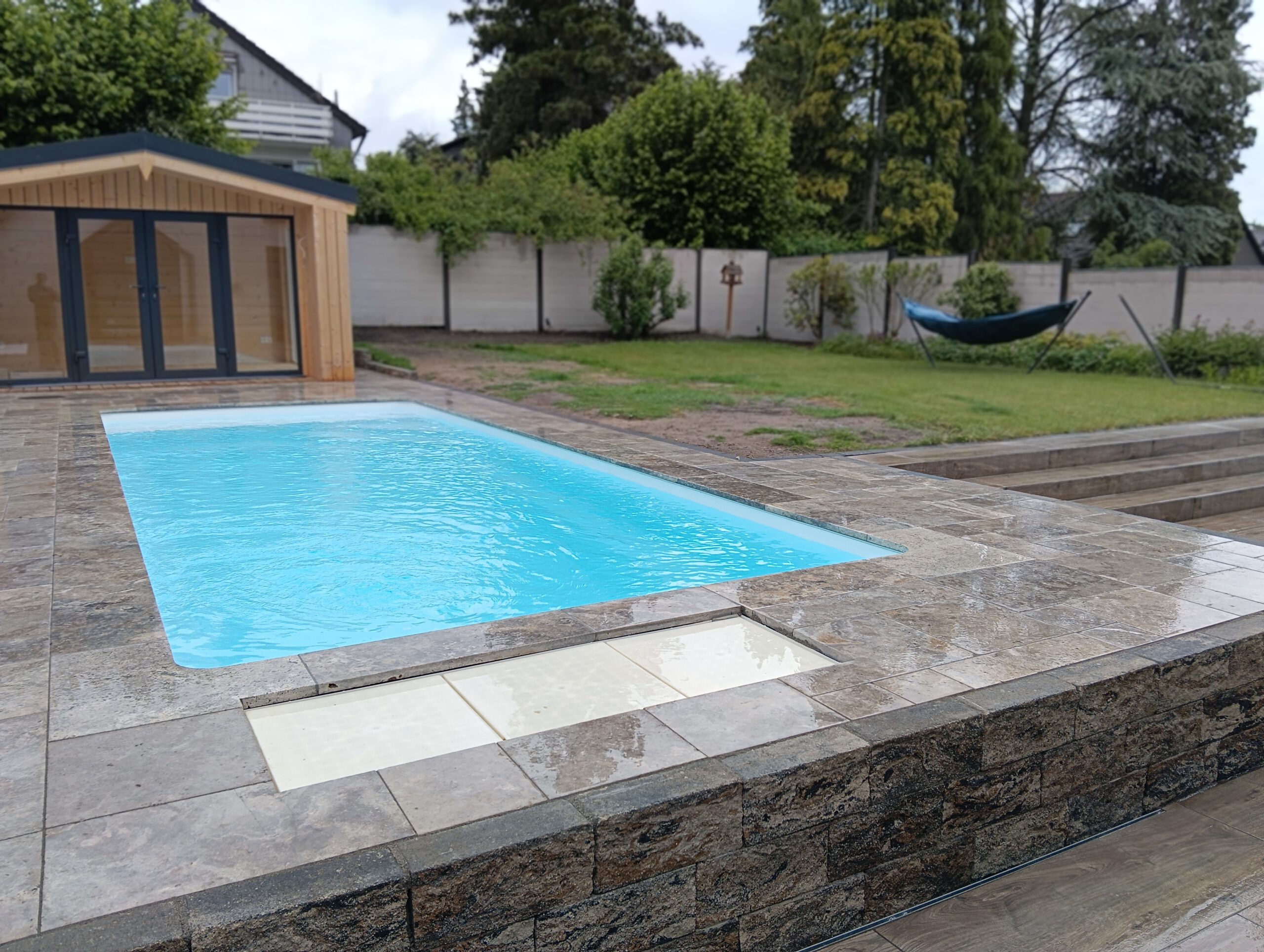 Swimmingpool mit Natursteineinfassung, gepflasterter Terrasse und Natursteinmauer im Garten